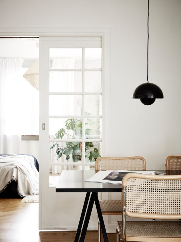 En matsal med bord och stolar. framför en äldre skjutdörrar med glas och spröjs. En flowerpot lampa hänger ovanför