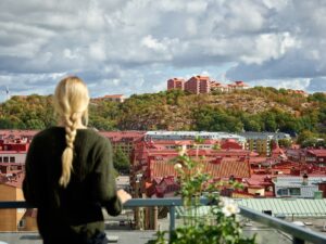 Kvinna med hästsvans blickar ut över stad från balkong.