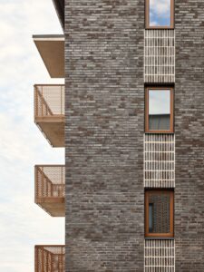 Detaljbild på arkitektur, mörkt tegel balkonger och fönster med gul karm.